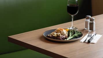 A plate of food with a glass of red wine, salt and pepper shakers, and cutlery on a wooden table.