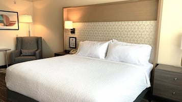 A hotel room with a large bed, a chair, a nightstand with a lamp, and a framed picture on the wall.