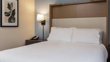 Una cama bien hecha con sábanas blancas, un cabecero de madera con diseño geométrico, una lámpara de noche e impresión enmarcadas de motivos botánicos en la pared.