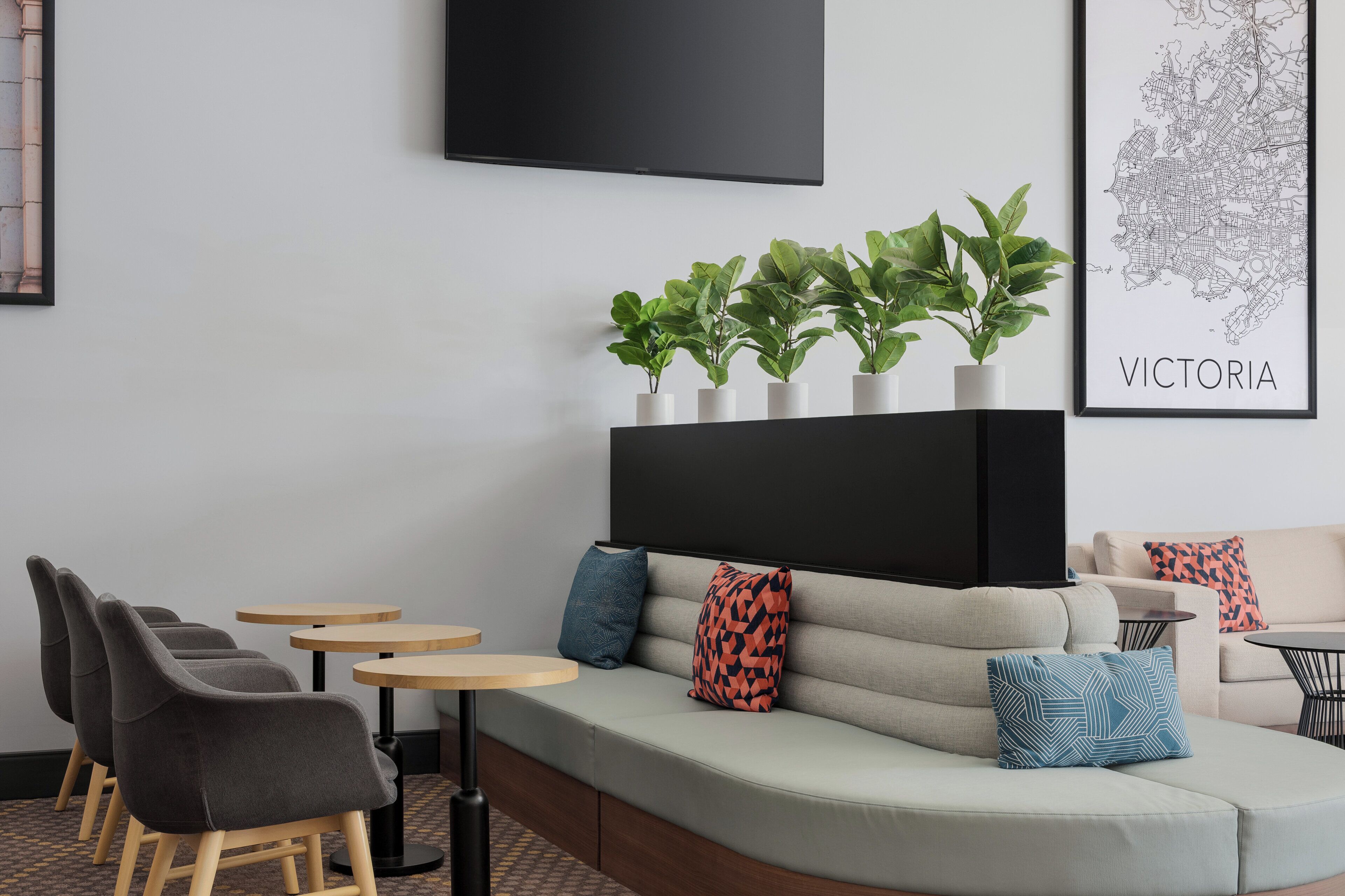 Un área de descanso moderna con sofá, sillas, mesitas y un televisor grande montado en la pared.
