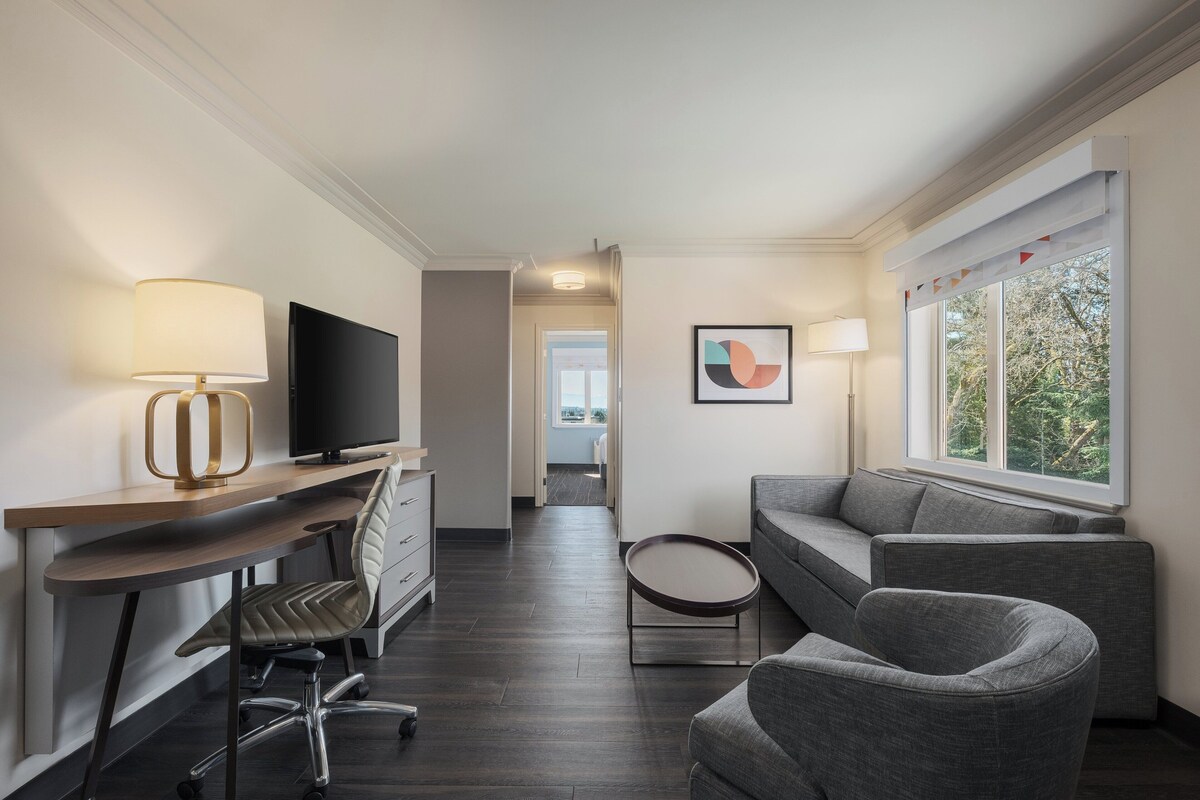 Een moderne hotelkamer met een bureau, stoel, televisie, bank en een raam met uitzicht.