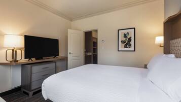 A hotel room with a bed, a television on a stand, a desk with drawers, a door to a closet, and a framed picture on the wall.