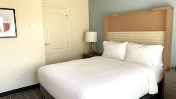 A hotel room with a bed, a nightstand, a lamp, and a door.