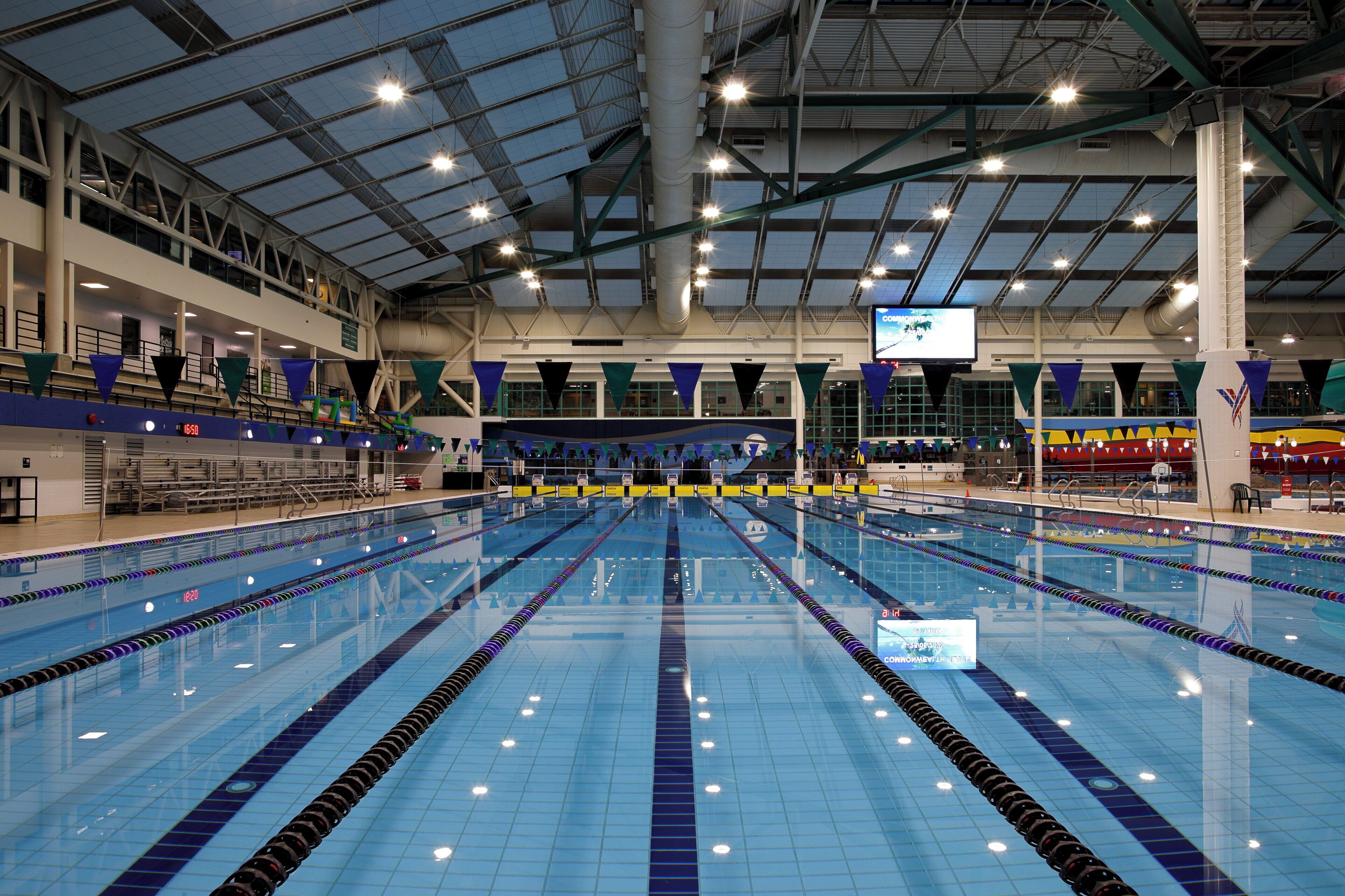 A large indoor swimming pool with multiple lanes, spectator seating, and a high ceiling with industrial lighting.