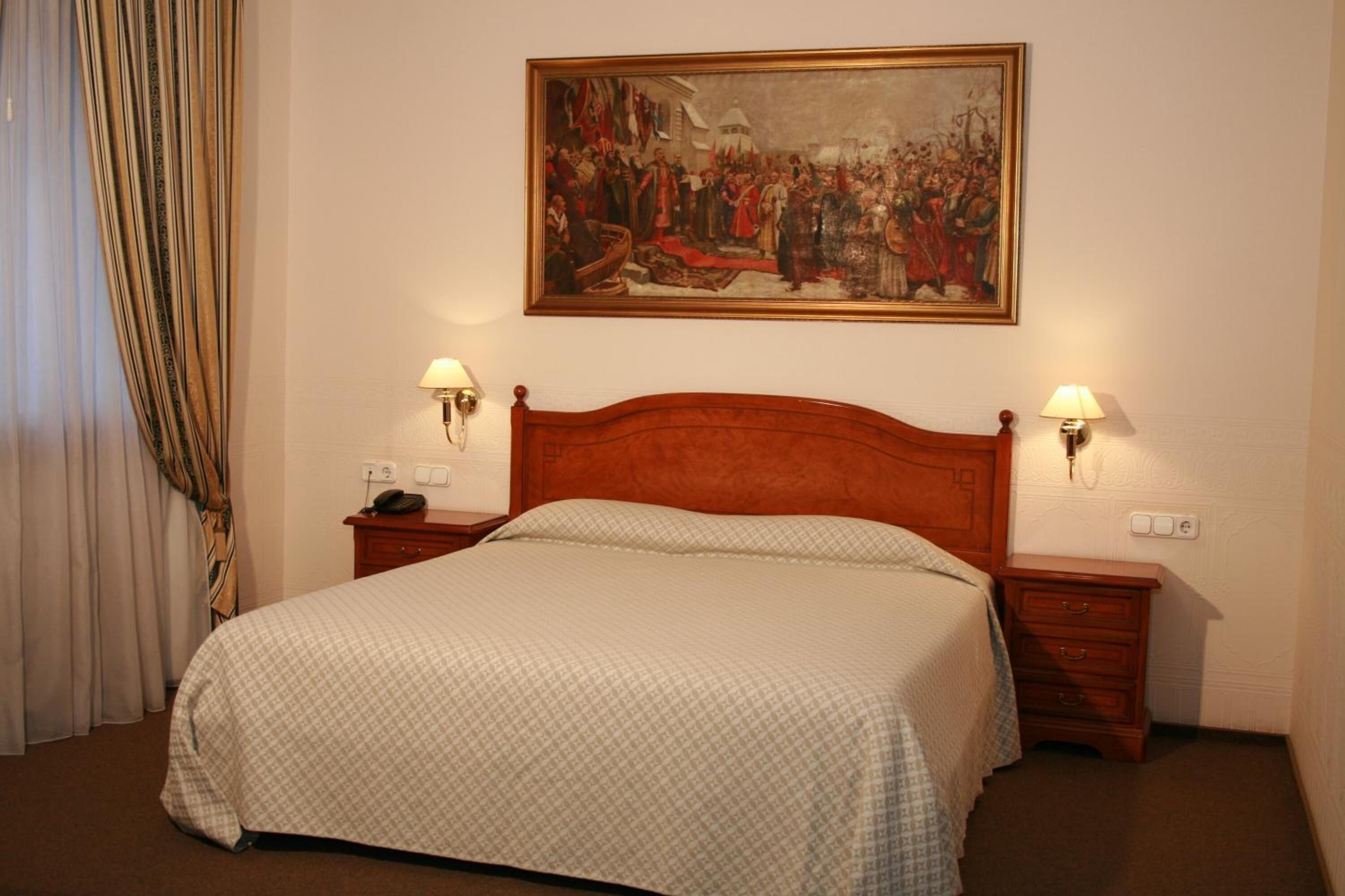 A hotel room with a large bed, two bedside tables with lamps, a painting on the wall, and a curtain on the window.