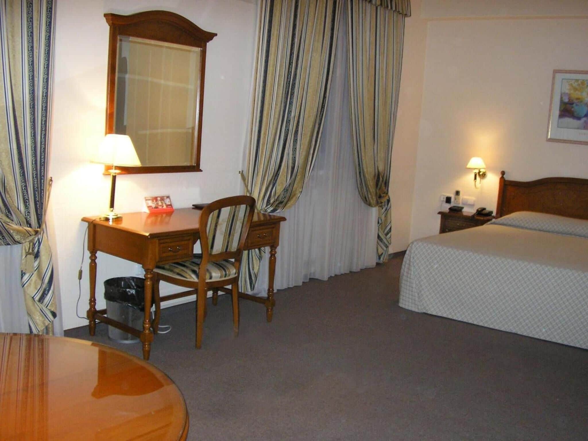 Una habitación de hotel con escritorio, silla, cama y mesita de noche con lámpara.