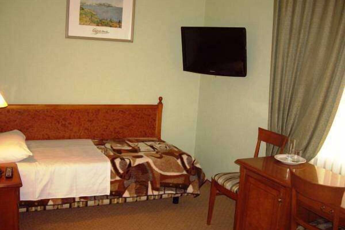 A hotel room with a bed, a television mounted on the wall, a desk with a chair, and a window with curtains.