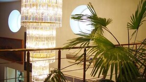 Un lustre à plusieurs niveaux, orné de cristaux, un grand miroir rond et une plante en pot aux longues feuilles.