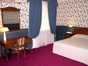 A hotel room with a bed, a desk with a chair, a mirror, a nightstand with a lamp, and a window with curtains. - Hotel Academy (Dnipro)