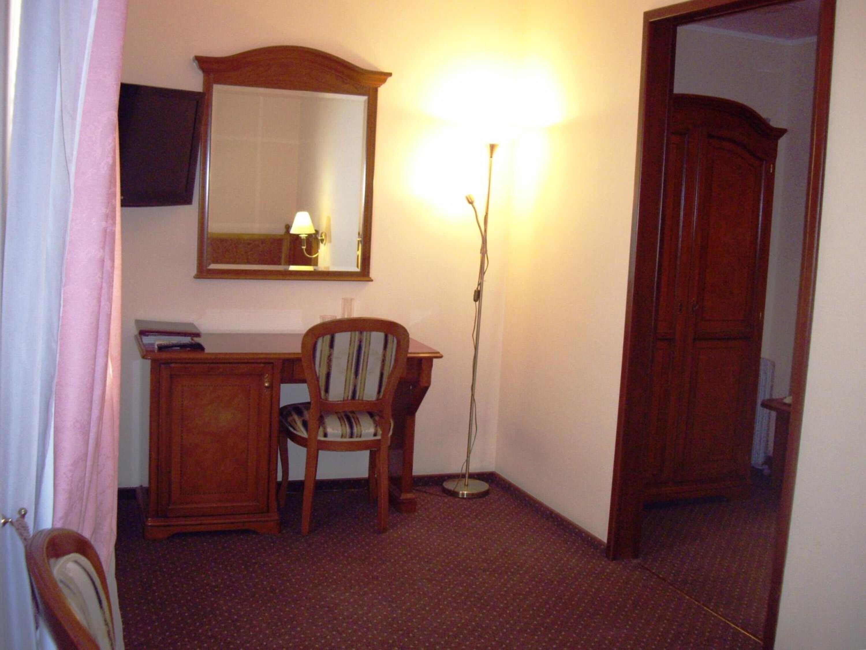 A room with a wooden desk, a chair, a mirror, and a floor lamp.