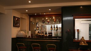 Un coin bar avec trois tabourets, un comptoir où sont exposées différentes bouteilles et une statue posée sur une table en bois.