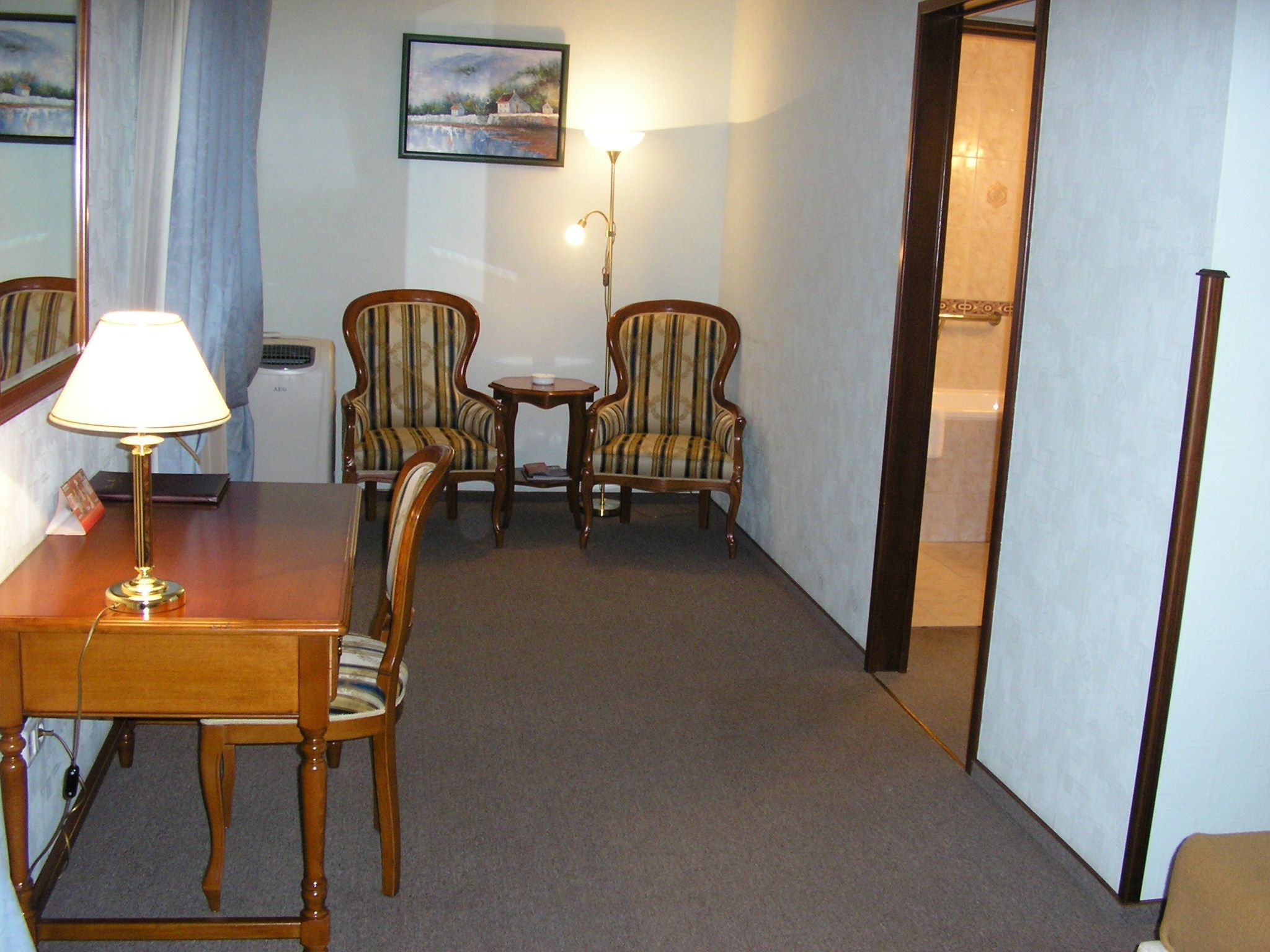 Een hotelkamer met een houten eettafel, twee gestreepte fauteuils, een klein bijzettafeltje en een lamp.