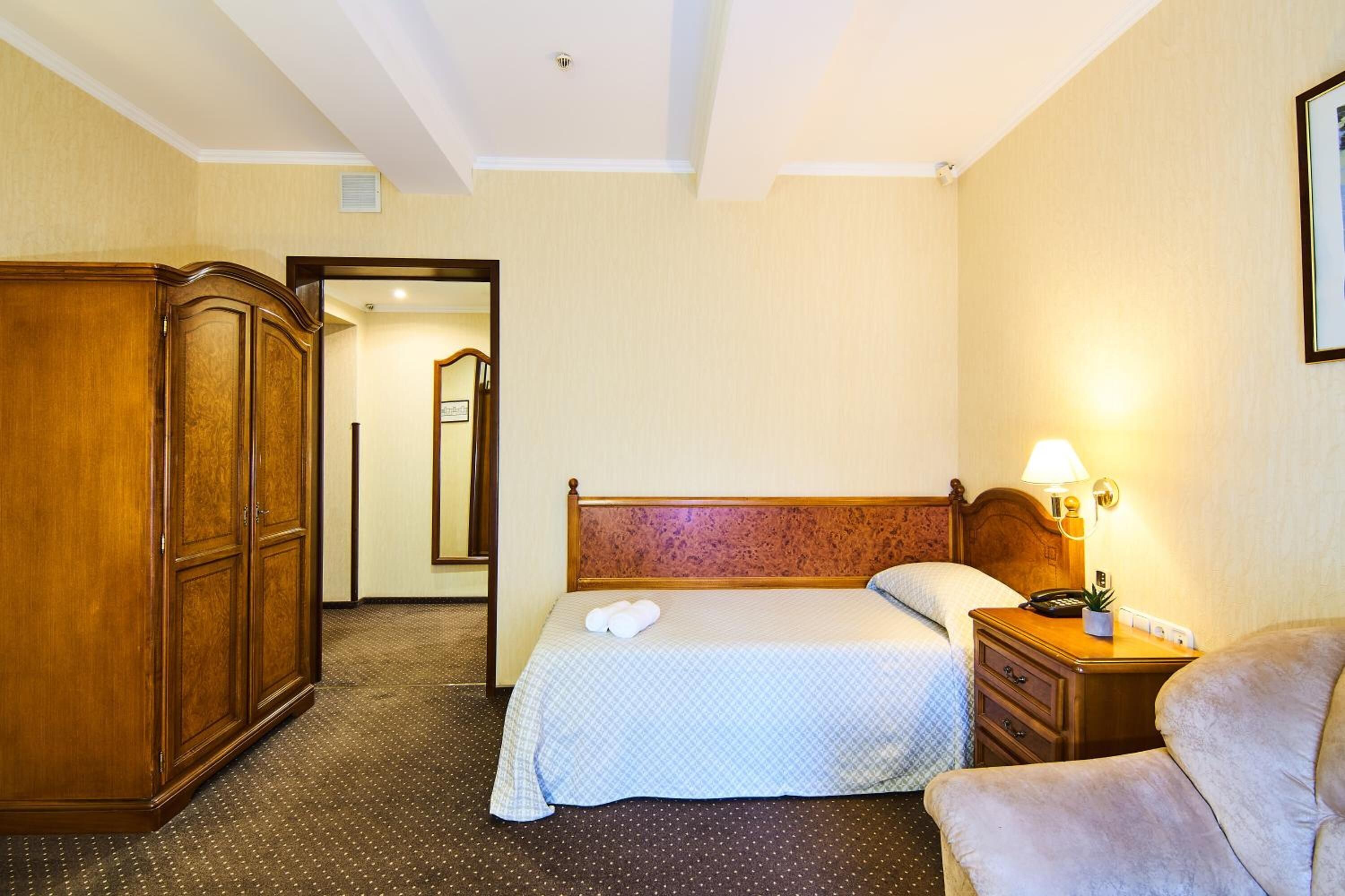 A hotel room with a bed, a wardrobe, a nightstand, and a chair.