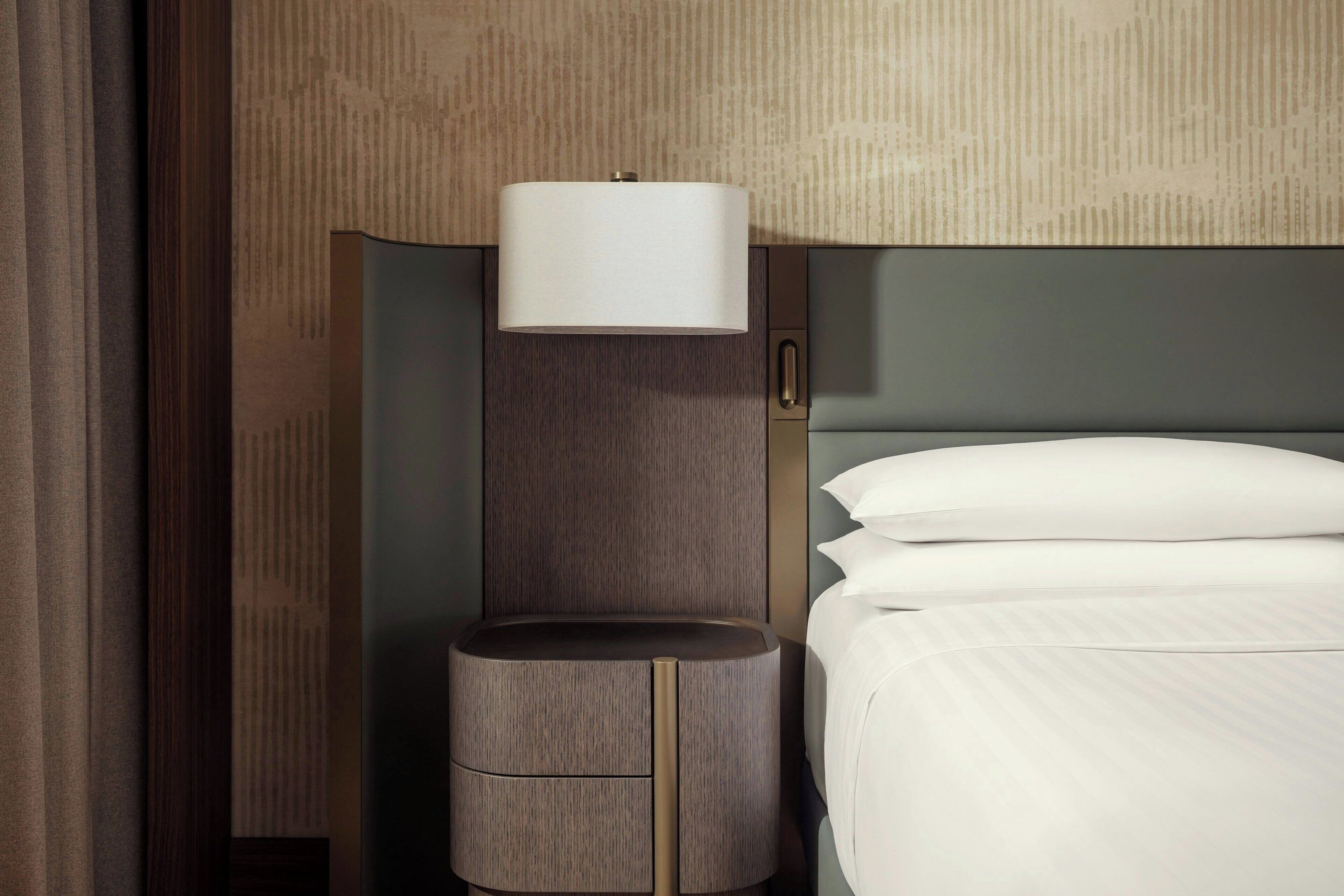 Una camera d'albergo con un letto, un comodino, una lampada e una parete con motivo decorativo.