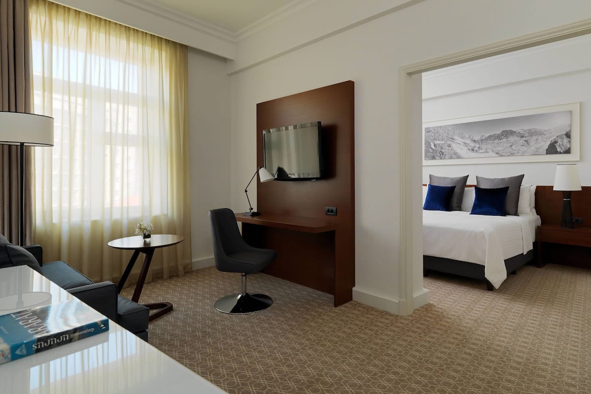 Ein Hotelzimmer mit einem Bett, einem Schreibtisch mit Stuhl, einem an der Wand befestigten Fernseher und einem kleinen Tisch mit Lampe.
