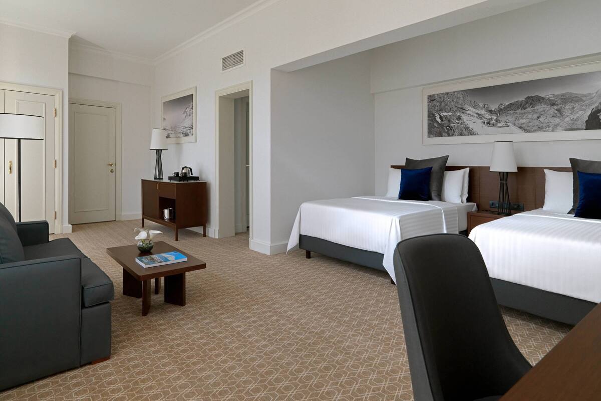 Ein Hotelzimmer mit zwei Betten, einem Schlafsofa, einem kleinen Tisch und einem Bild an der Wand.