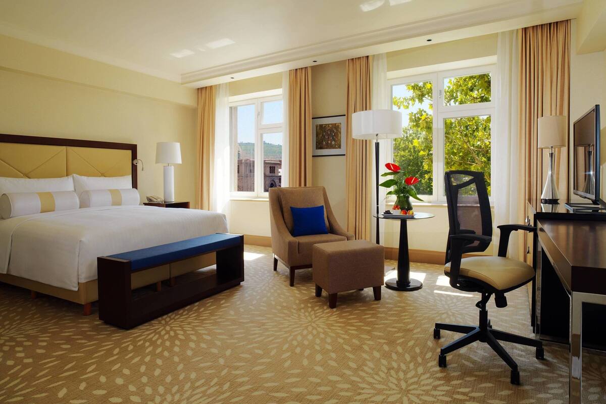 Ein Hotelzimmer mit einem großen Bett, einem Schreibtisch, einem Stuhl und einem kleinen Tisch mit Blumen in einer Vase.