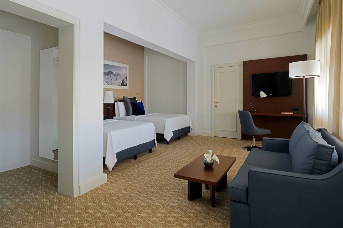 Ein Hotelzimmer mit zwei Betten, einem Sofa, einem Fernseher und einer Lampe.