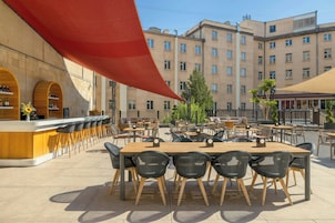 Een terras met een houten tafel en stoelen, omgeven door een rode luifel.
