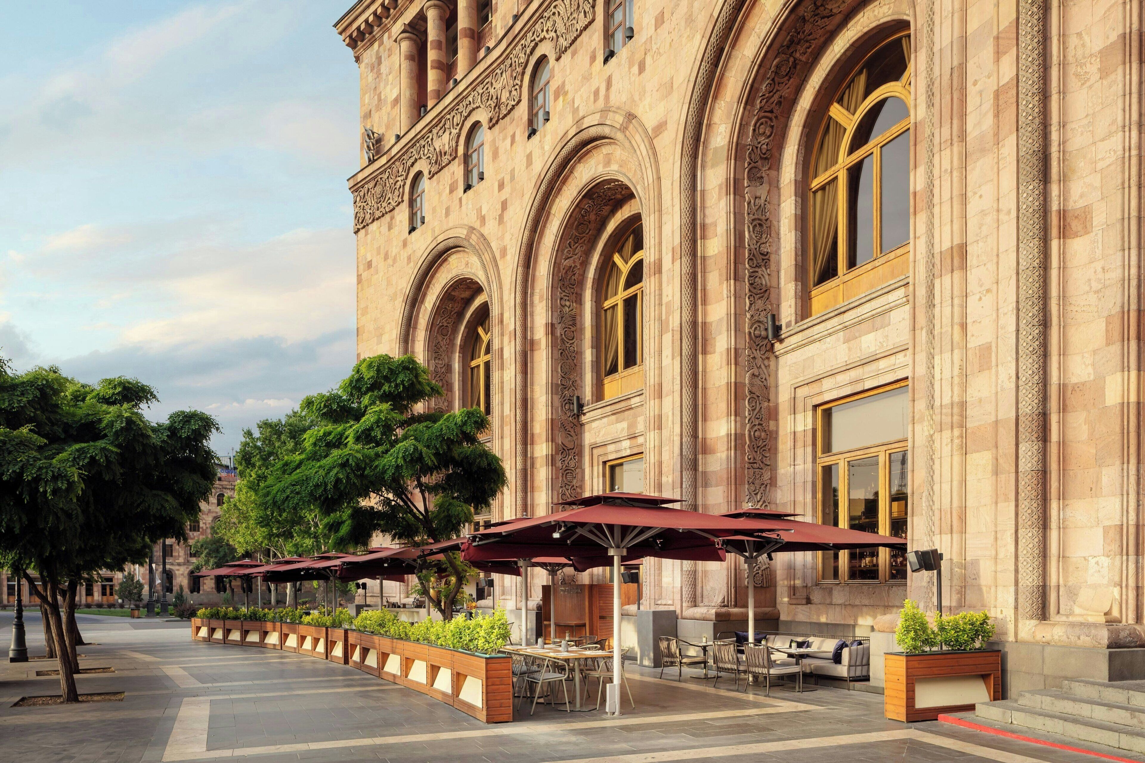 A building with ornate architecture, outdoor seating with umbrellas, and a paved walkway.