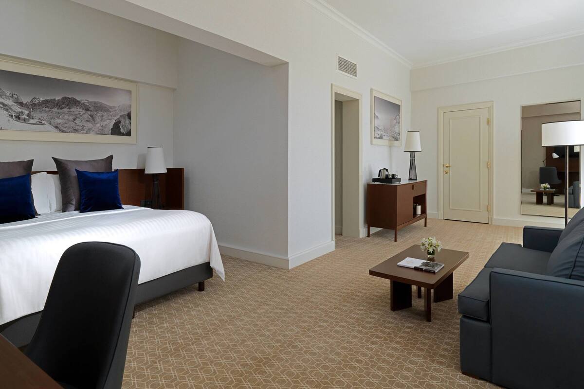 Ein Hotelzimmer mit Bett, Schreibtisch, Stuhl, Sofa, Couchtisch und Kommode.