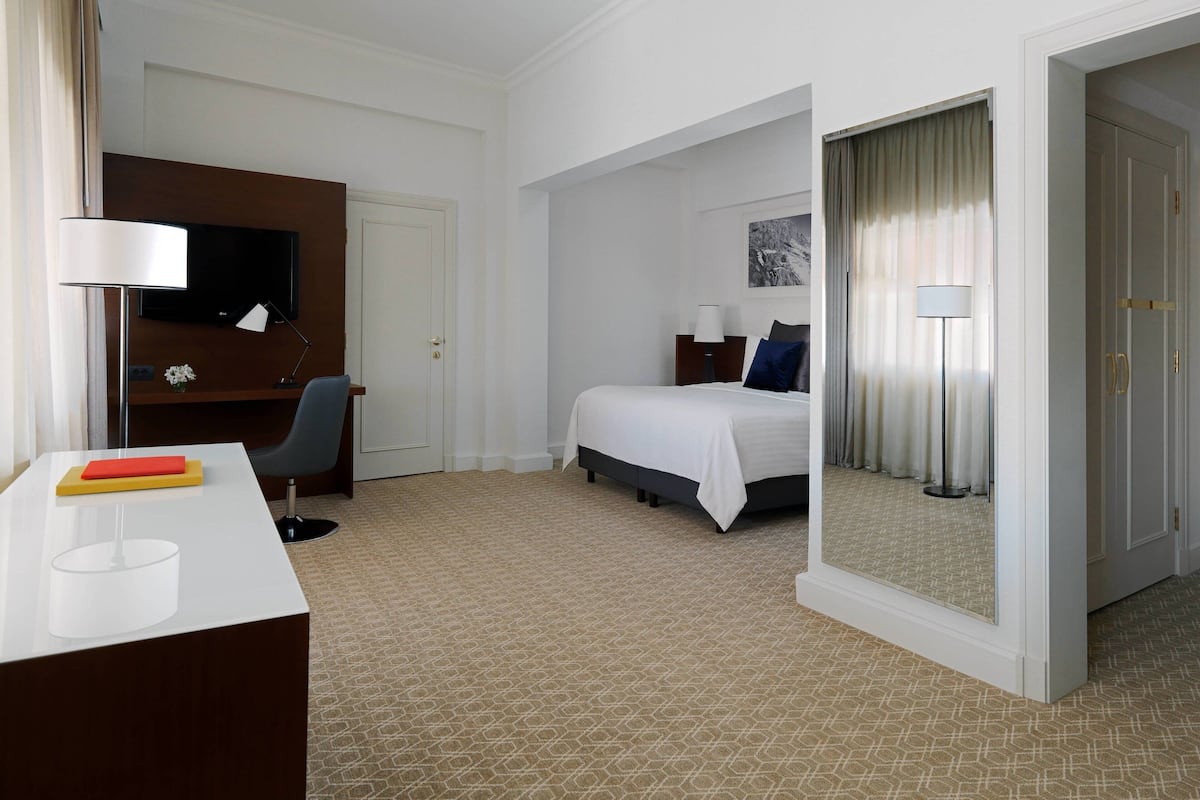 Ein Hotelzimmer mit Bett, Schreibtisch mit Lampe, Fernseher und Spiegel.