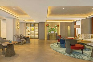 Een moderne hotellobby met een receptiebalie, een zithoek en een plantenpresentatie.