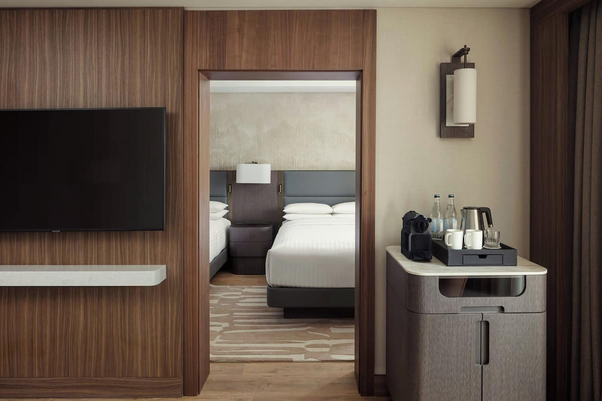 A hotel room with a TV, a bed, a desk with a coffee maker, and a minibar.