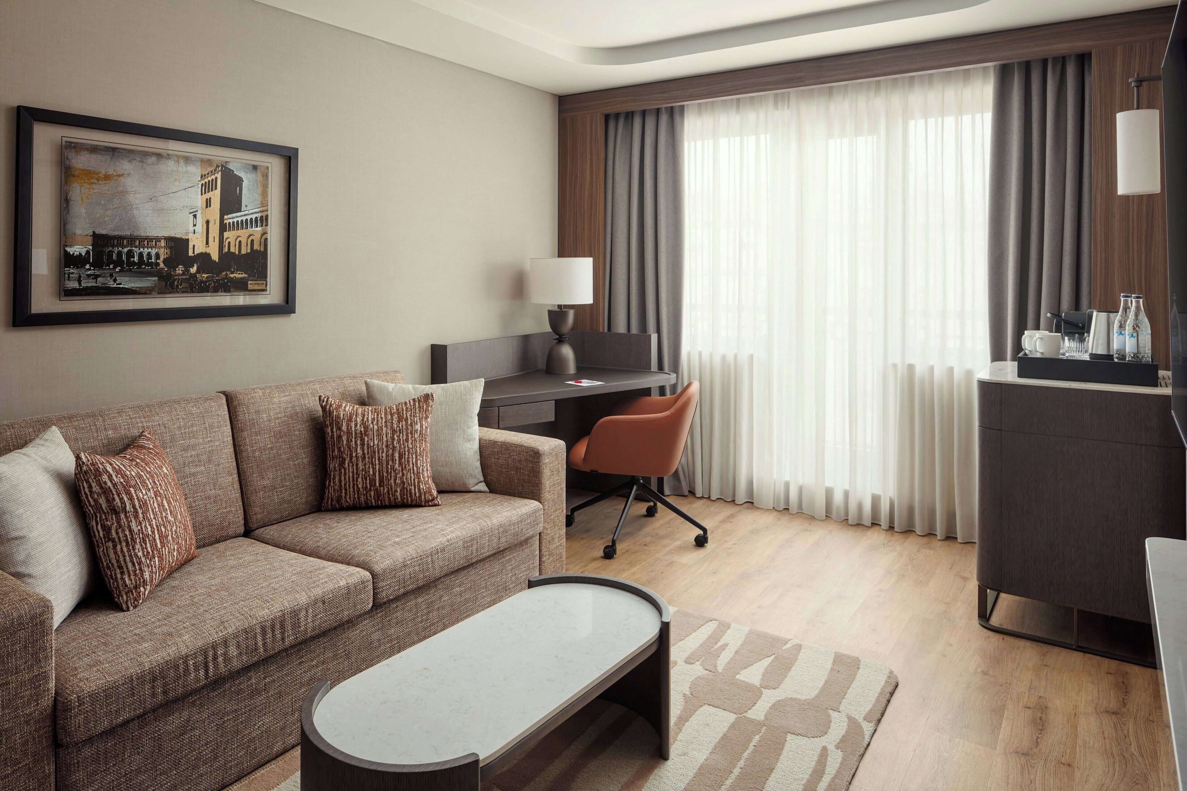 Une chambre d’hôtel moderne, équipée d’un canapé, d’un bureau, d’une chaise et ornée d’un tableau au mur.