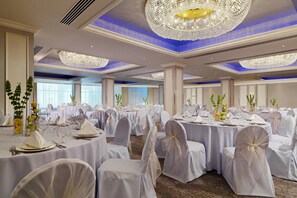 Banquet hall with round tables set for dining, featuring classic architectural design and ornate chandeliers.