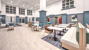 A spacious lobby with multiple seating areas, including a long bench and several tables and chairs. - Hampton Inn & Suites by Hilton West Little Rock (Little Rock)