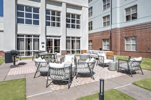 Un patio al aire libre con mobiliario de mimbre, una parrilla y un edificio de ladrillo al fondo.