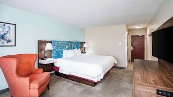 Una habitación de hotel con cama, sillón, televisor y escritorio.