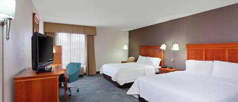 A hotel room with two beds, a desk with a television, a chair, and a lamp.