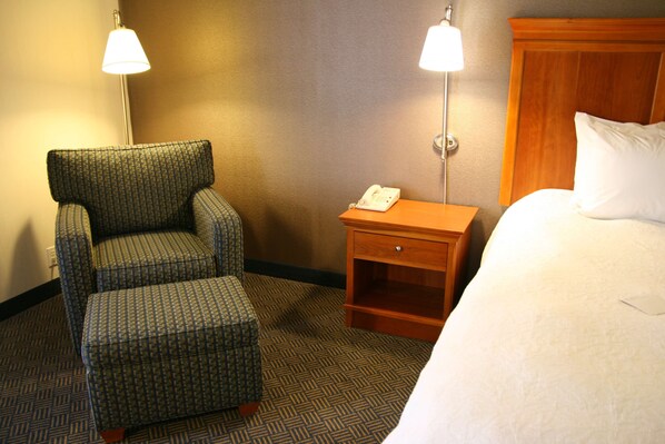 A hotel room with a bed, a chair, a nightstand with a phone, and two wall lamps.
