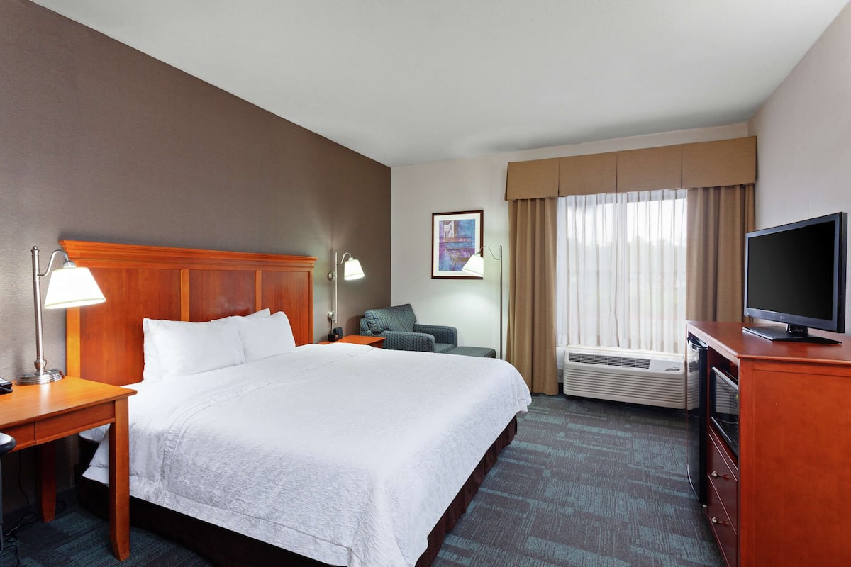 Habitación de hotel con una cama grande, un escritorio con lámpara, una silla, un televisor y un aire acondicionado.