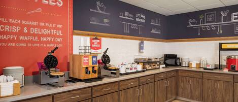 A kitchen area with waffle-making equipment, a coffee station, and a caution sign for hot surfaces.