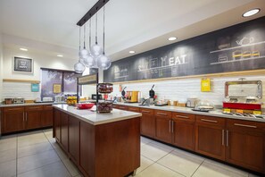 A modern kitchen with wooden cabinets, a central island, and a black backsplash with 'EAT' written on it.