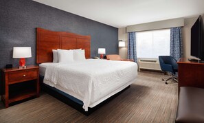 A hotel room with a large bed, two bedside tables with lamps, a desk with a chair, and a large window with curtains.