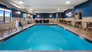An indoor swimming pool with clear blue water, surrounded by lounge chairs and tables, and a view of the outside through large windows. - Hampton Inn Medford (Medford)