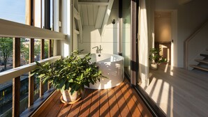 Un baño moderno con una bañera independiente, una planta en maceta y vistas de la ciudad a través de amplias ventanas.