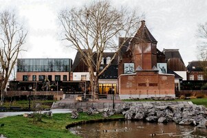 Ein Hotel mit einem traditionellen Backsteinturm, einem modernen Glasgebäude und einem Teich mit Enten.
