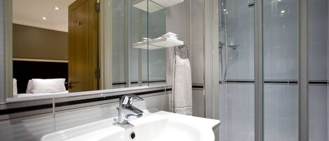 Un baño moderno con cabina de ducha de vidrio, lavamanos blanco y un espejo grande que refleja el ambiente.