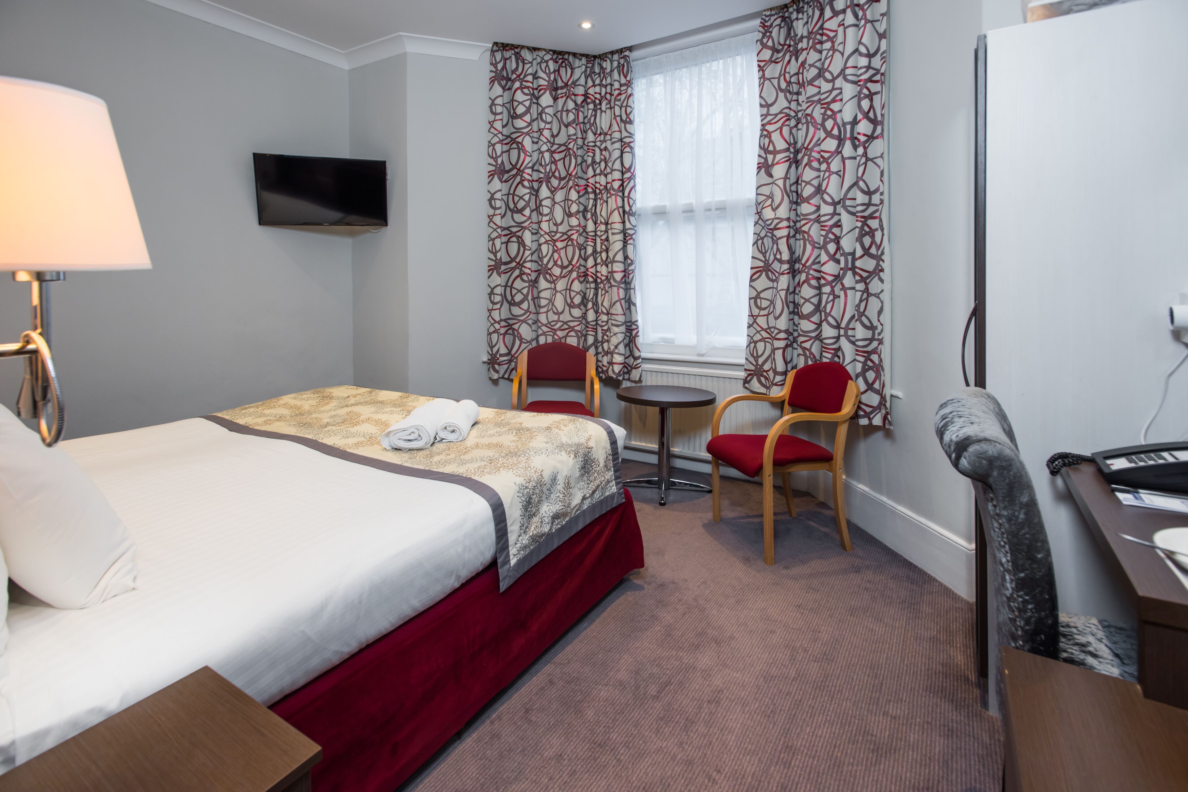 Ein Hotelzimmer mit einem Bett, einem Schreibtisch mit Tastatur, einem Sessel, einem kleinen Tisch und einem an der Wand befestigten Fernseher.