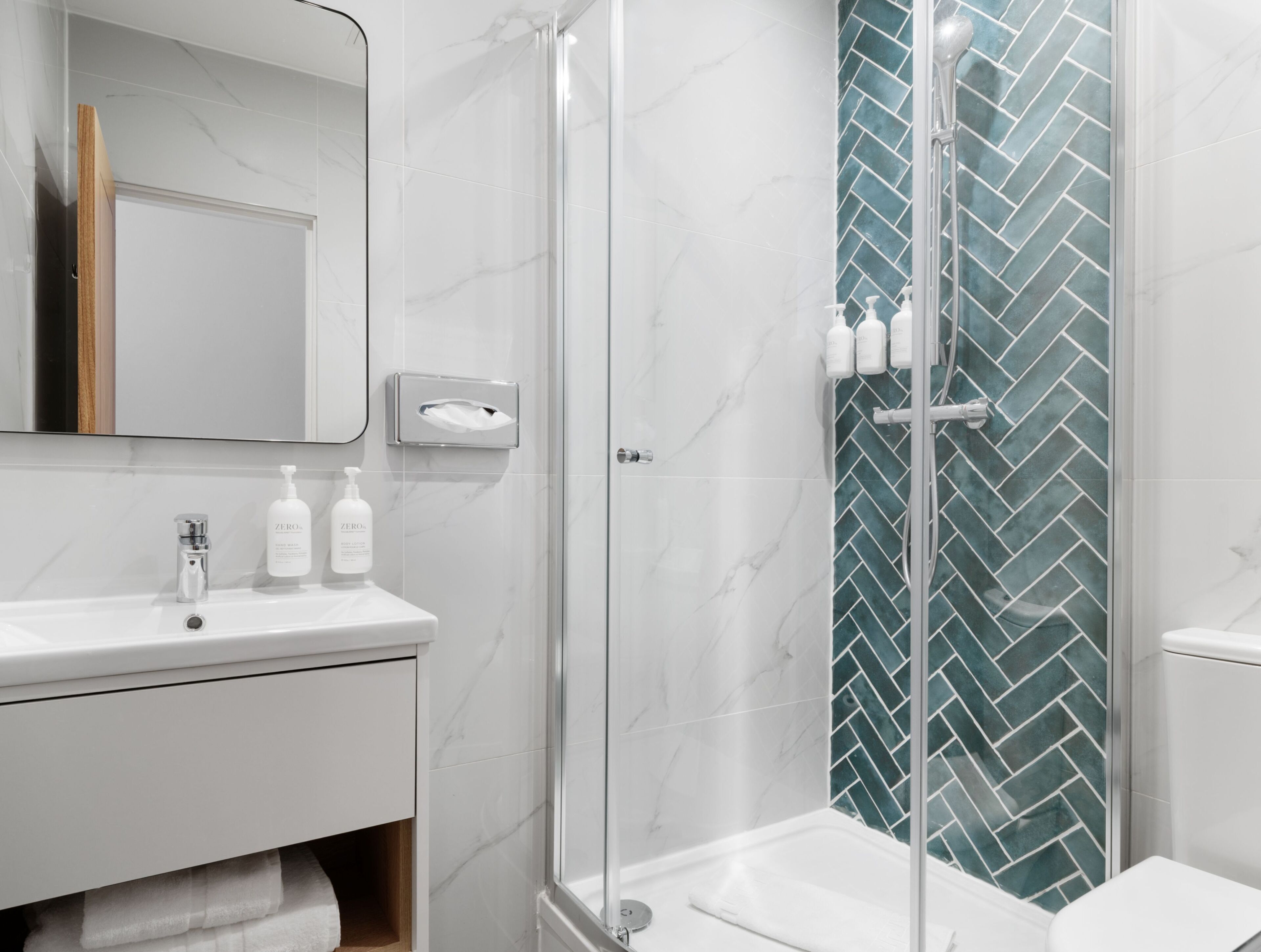 Une salle de bain moderne avec une douche à parois de verre, un lavabo blanc et un miroir au-dessus.
