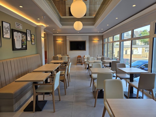 A modern restaurant with booths and tables, large windows, and wall-mounted artwork.