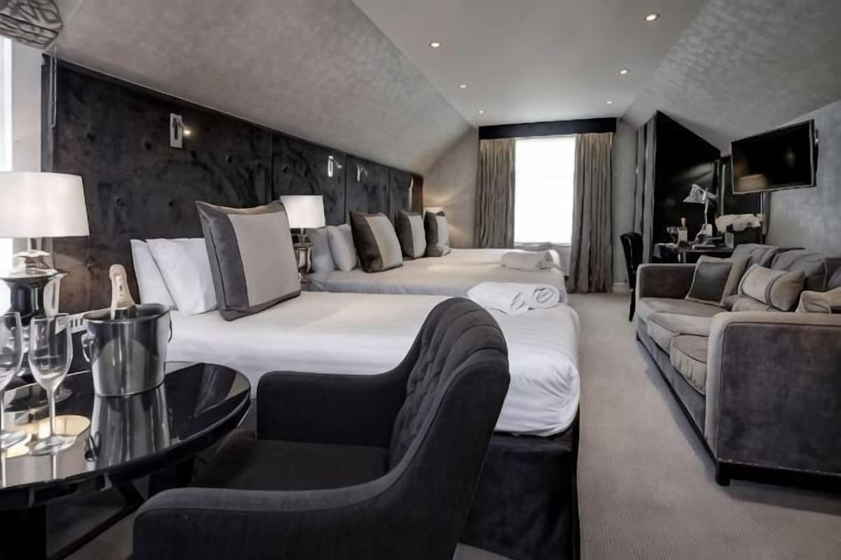 A hotel room with two beds, a sofa, a dining table, and a TV.