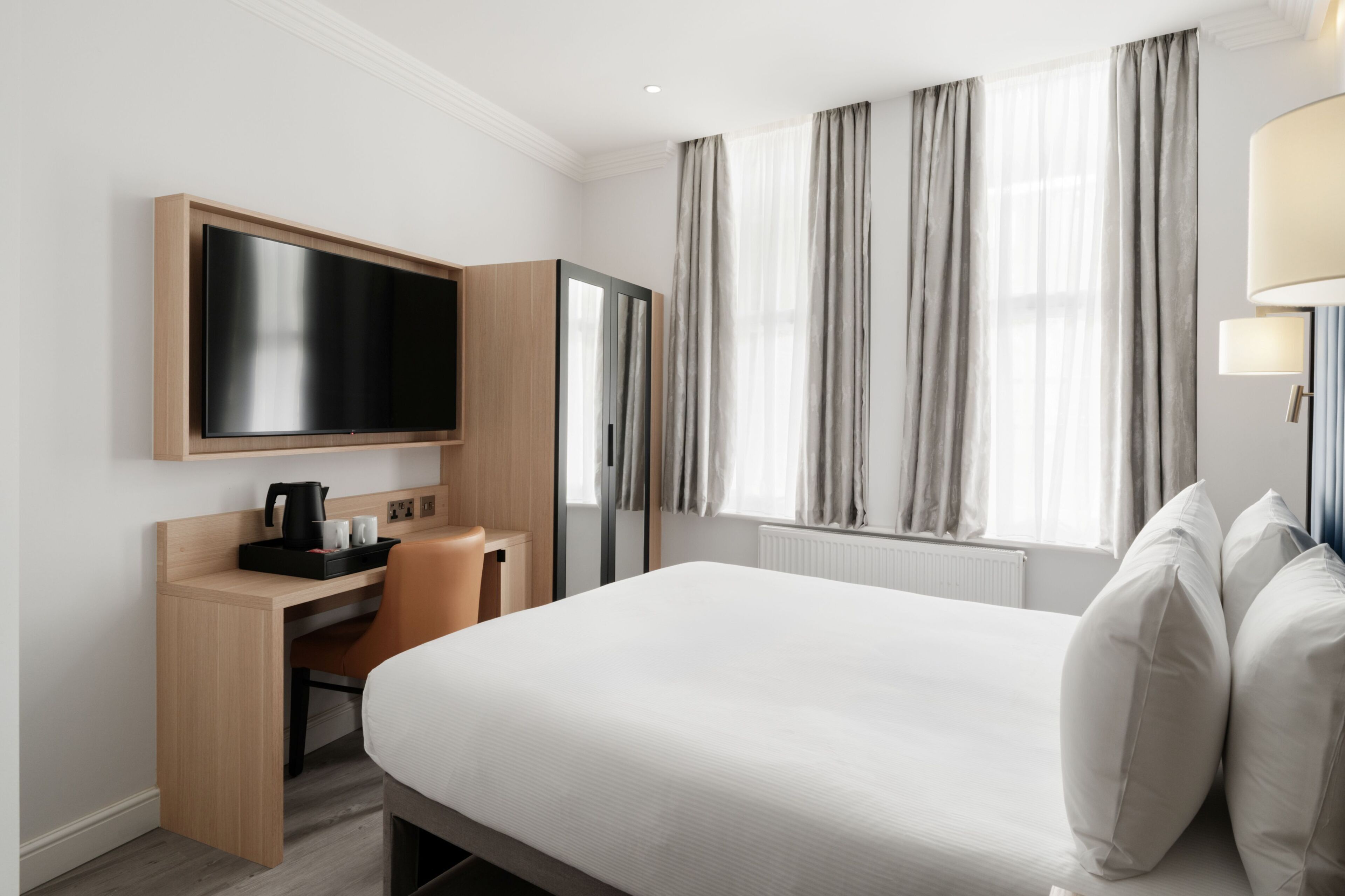A hotel room with a bed, a desk with a flat-screen TV, a coffee maker, and a wardrobe.