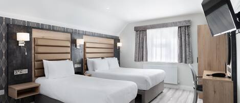 A hotel room with two beds, a TV, a desk, and a window with curtains.