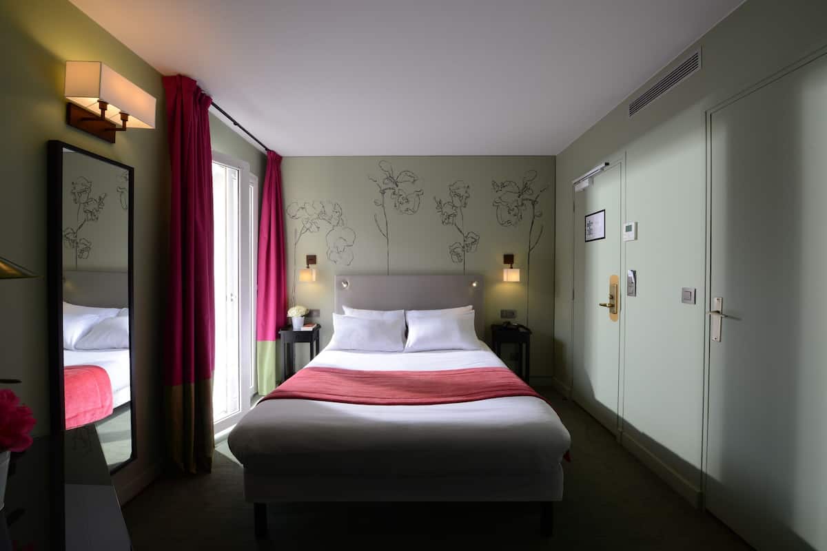Una habitación de hotel con una cama grande, una mesita de noche, un espejo, un armario y un tocador.